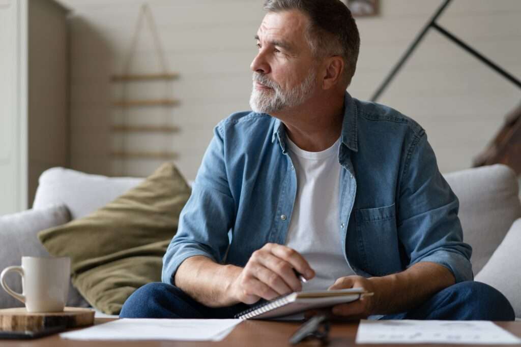 older man looking at something outside, holding a pen and notebook