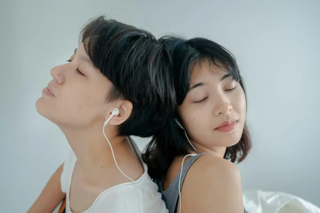 A male and female partner sit back-to-back with earbuds in, representing sensory-friendly intimacy and the balance between connection and personal space in neurodivergent relationships.