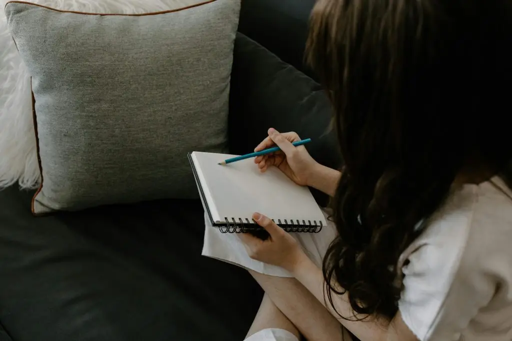 A person sitting on a couch writing in a journal, reflecting and preparing for a first therapy session