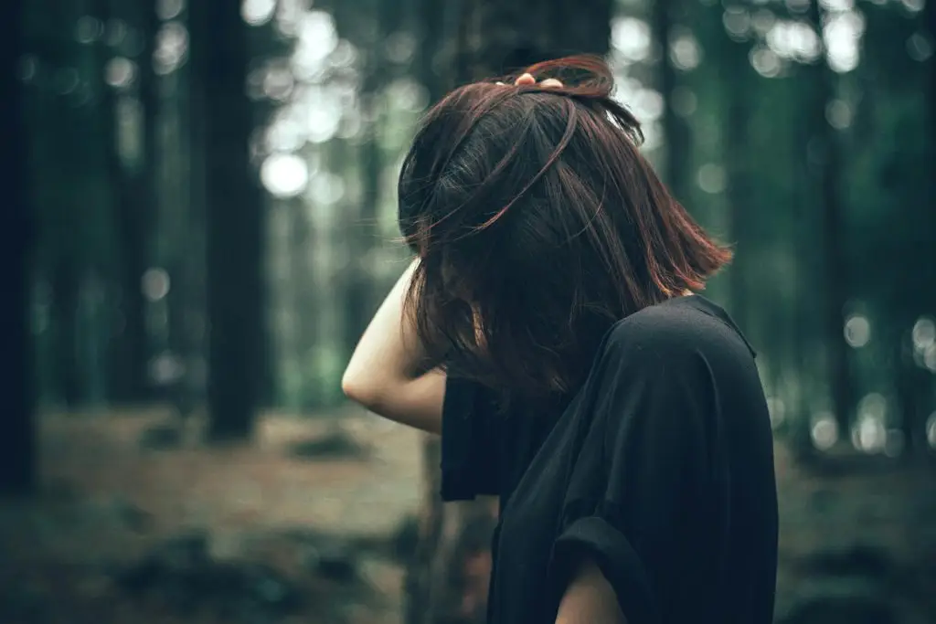 Woman standing in a forest with head down, representing overthinking, anxiety, and emotional overwhelm